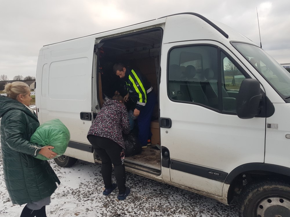 Osoby ładujące do białego busa używaną odzież spakowaną w worki