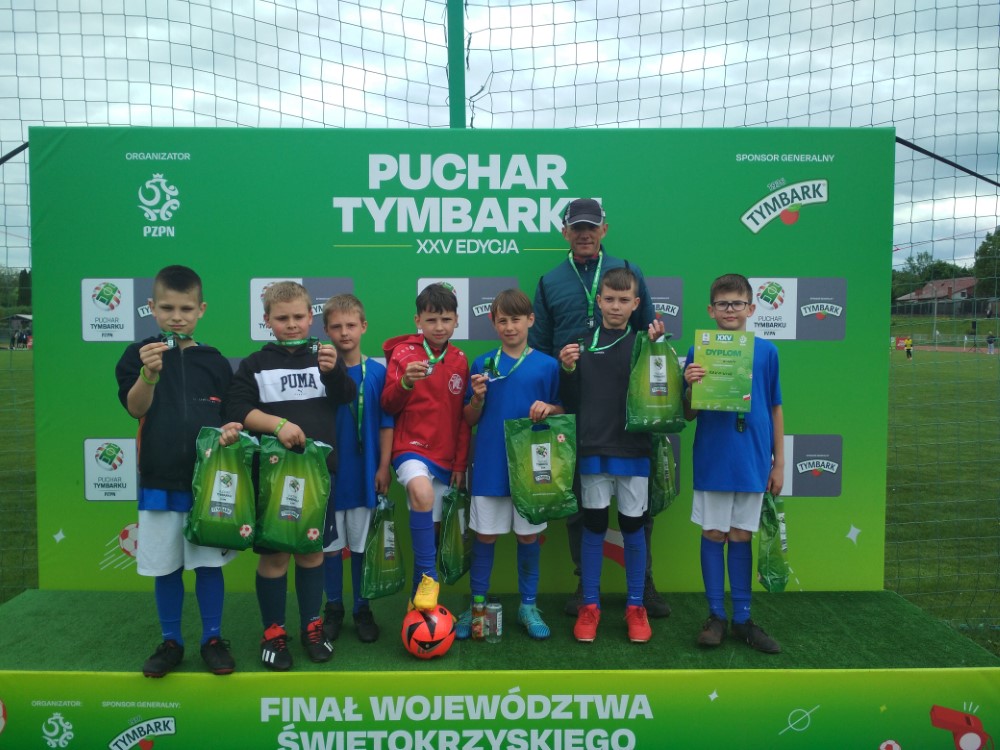 Zdjęcie grupowe ośmiu osób na tle baneru z napisem Puchar Tymbarku
